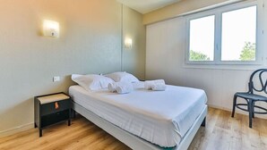 Ein Schlafzimmer mit Bett, Nachttisch, Sessel und einem Fenster mit Tageslicht.