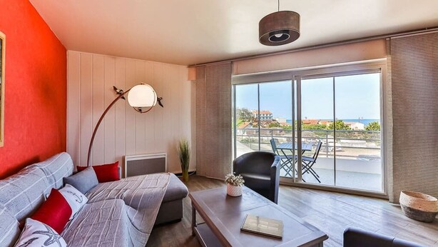 Ein modernes Wohnzimmer mit einer Couch, einem Couchtisch und einem Essbereich mit Tisch und Stühlen. Ein großes Fenster bietet einen Ausblick nach draußen.