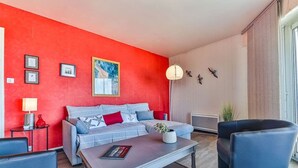 Ein modernes Wohnzimmer mit roter Akzentwand, einem grauen Sofa mit gemusterten Kissen, einem Couchtisch mit einem Buch und einem schwarzen Sessel.