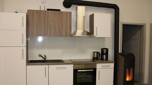 A modern kitchen with white cabinets, a stainless steel oven, a coffee maker, and a wood-burning stove. - Bungalow on the Ostalb<br> (Eschach)