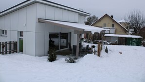 A modern house with a covered patio, a fenced yard, and a snow-covered roof. - Bungalow on the Ostalb<br> (Eschach)