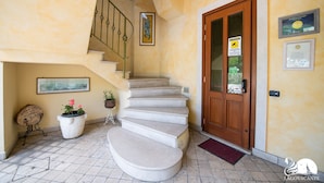 A staircase leading to a wooden door with a sign, a welcome sign, and a framed picture on the wall. - Feeling House (Salò)