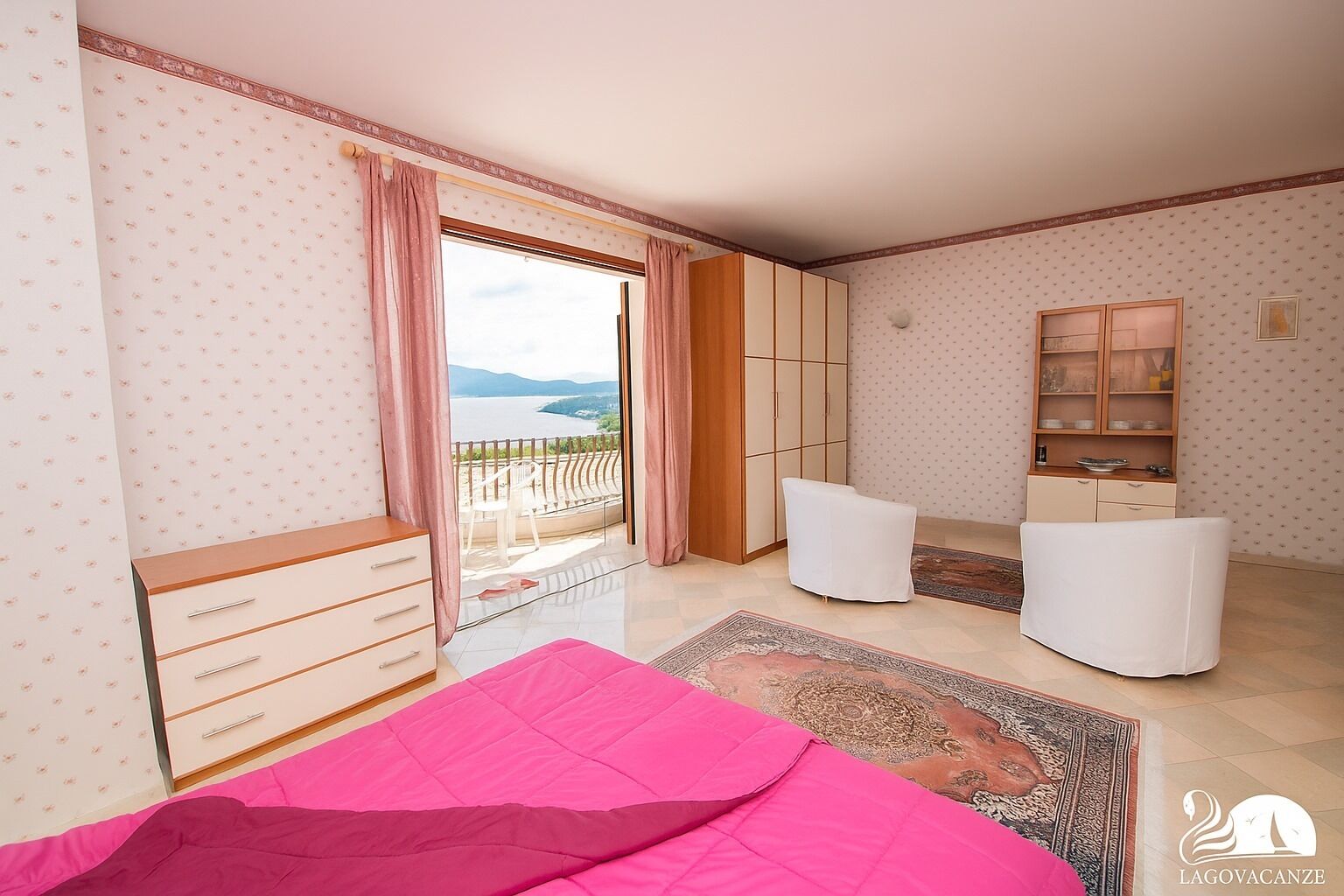 A bedroom with a bed, a wardrobe, a seating area, and a view of the sea.