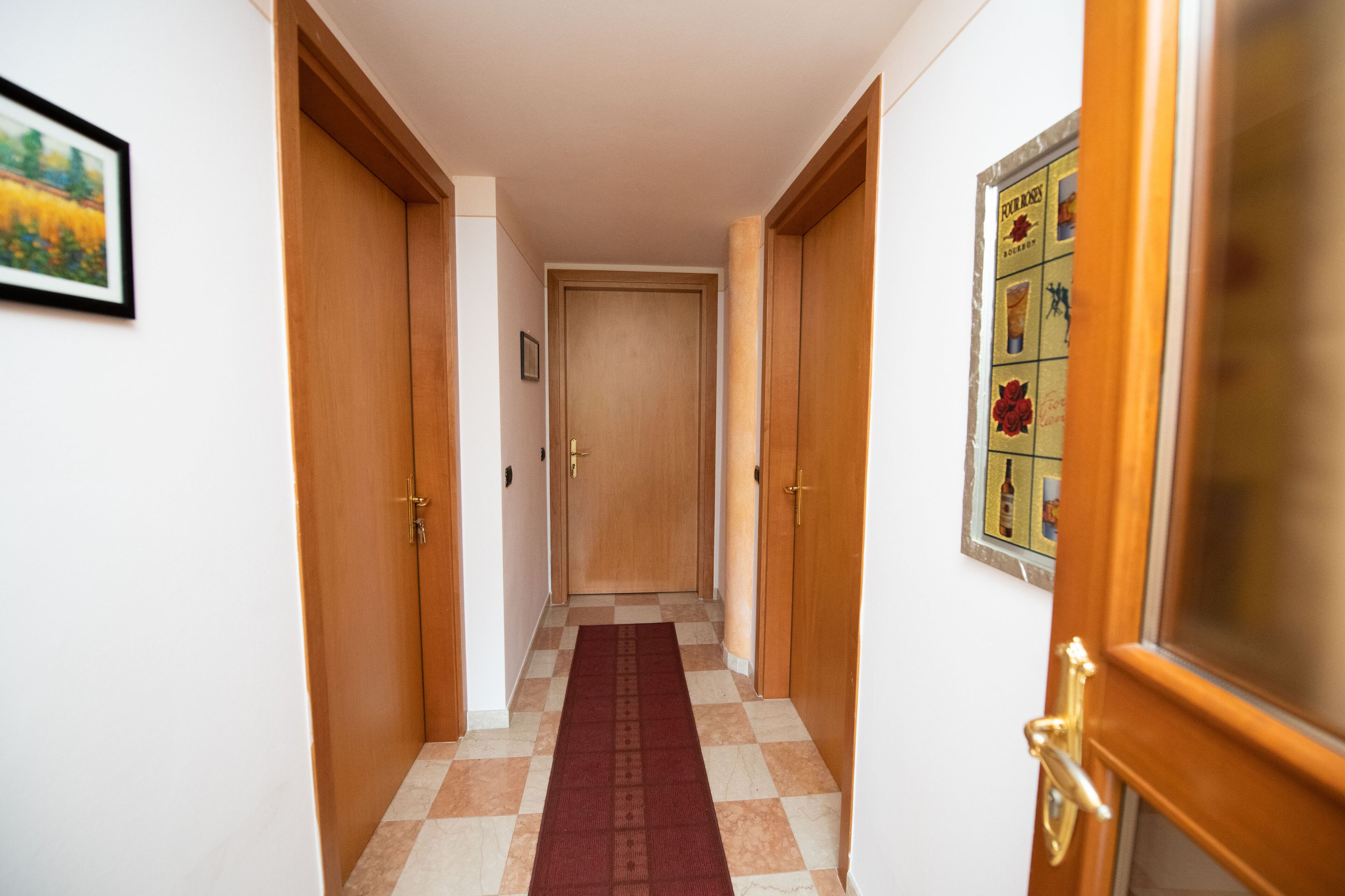 A hallway with wooden doors, a checkered floor, and a framed picture on the wall.