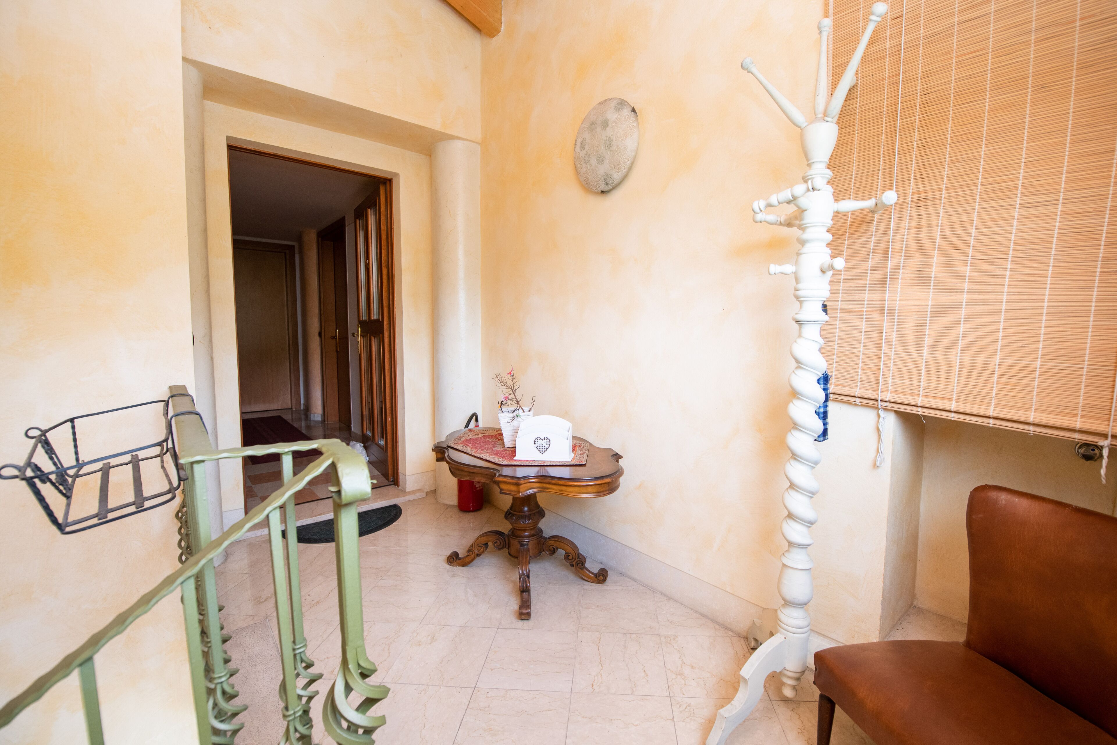 A hallway with a wooden chair, a small table with a decorative item, and a metal rack.