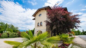 A building with a tower, surrounded by greenery and a clear sky. - Feeling House (Salò)