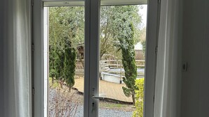 Une porte double donnant sur un jardin et une terrasse en bois à l’extérieur.