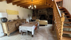 A rustic interior with a wooden staircase, a stone fireplace, a dining area with a table and chairs, and a sofa. - Maison en Granit Typique Rénovée (Plounévez-Moëdec)