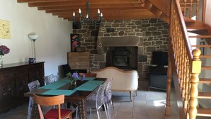 A dining area with a wooden table, chairs, and a chandelier. There is a stone fireplace and a wooden staircase. - Maison en Granit Typique Rénovée (Plounévez-Moëdec)