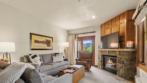 Una sala de estar con un sofá gris, un sillón marrón, una chimenea y un televisor.