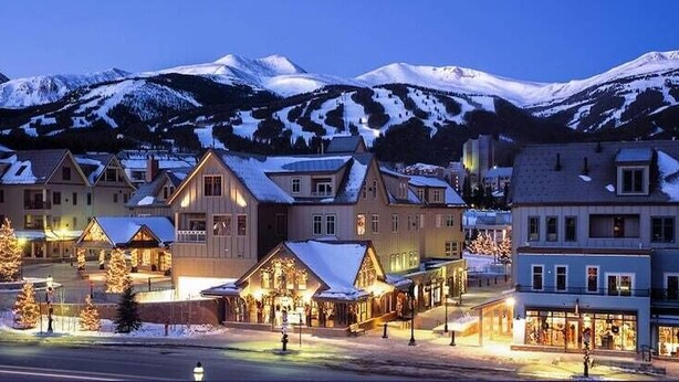 Un pueblo cubierto de nieve al anochecer, con edificios iluminados y una carretera en primer plano.