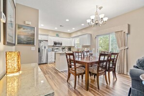 A spacious kitchen with white cabinets, a central island, and a dining area with wooden chairs and a glass table.