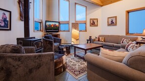 A cozy living room with a fireplace, comfortable seating, and large windows offering views of the outdoors. - 90ST1 | Dog Friendly | Private Hot Tub | Short Walk to Slopes | Winter Shuttle (Steamboat Springs)