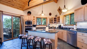 A modern kitchen with wooden cabinets, a central island with bar stools, and large windows offering views of the outdoors. - 90ST1 | Dog Friendly | Private Hot Tub | Short Walk to Slopes | Winter Shuttle (Steamboat Springs)