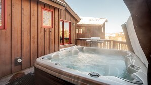 Eine Holzhütte mit Whirlpool, Terrasse und Blick auf eine verschneite Landschaft.