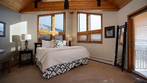 Ein Schlafzimmer mit einem Bett, zwei Nachttischen, einem Fenster mit Jalousien, einem Spiegel und einer Tür mit Blick ins Freie.