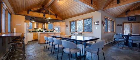 A spacious kitchen with a large island, wooden ceiling beams, and a view of the outdoors through large windows.