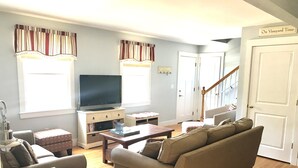 A living room with a sofa, a coffee table, a TV on a stand, and a staircase leading to another room. - Newly renovated, 4 bedroom, central location, Immaculate, bright Family Retreat! (edgartown)