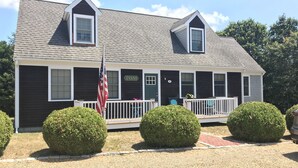 A two-story house with a dark exterior, a front porch with a railing, and a sign that reads "EVANS". - Newly renovated, 4 bedroom, central location, Immaculate, bright Family Retreat! (edgartown)