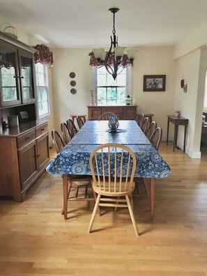 A dining room with a long table, wooden chairs, a chandelier, and a window with curtains.