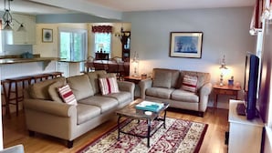 A living room with two sofas, a coffee table, and a TV stand. There is a dining area with a table and chairs in the background. - Newly renovated, 4 bedroom, central location, Immaculate, bright Family Retreat! (edgartown)