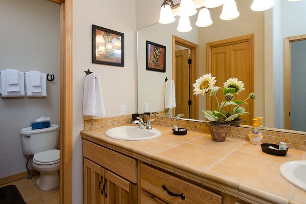 A bathroom with a double sink, a toilet, a mirror, and a vase with flowers.
