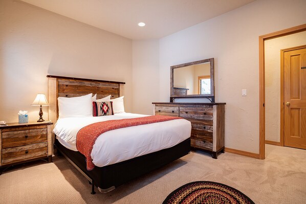 A bedroom with a large bed, wooden headboard, a dresser with a mirror, and a carpeted floor.