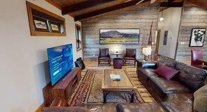 Una sala acogedora con televisor, sofá de cuero y un cuadro grande de un paisaje.