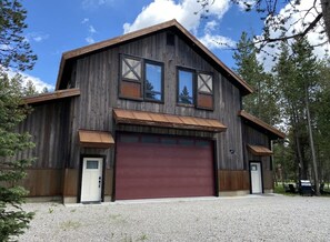 A two-story wooden building with a large garage door, large windows, and a sloped roof.