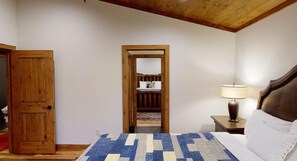 Ein Schlafzimmer mit Holztür, einem Bett mit gemustertem Überwurf, einem Nachttisch mit Lampe und einem Holz-Kopfteil.