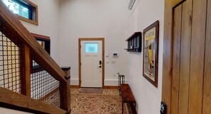A hallway with a wooden staircase, a white door with a light panel, a bench, and a framed picture on the wall.