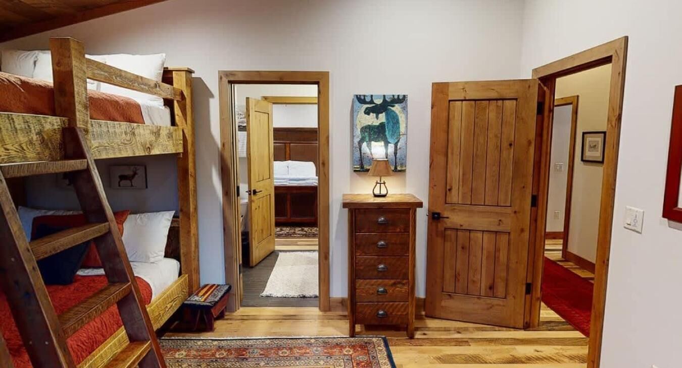 A room with bunk beds, a wooden dresser, and a door leading to another room.