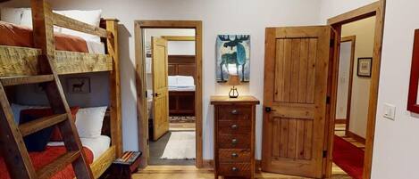 A room with bunk beds, a wooden dresser, and a door leading to another room.