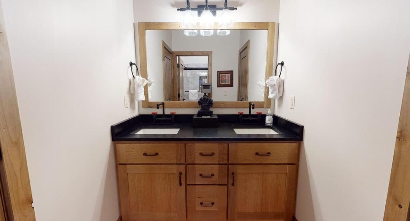 A bathroom with two sinks, a large mirror, and wooden cabinetry.