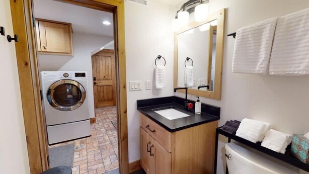 Ein kleines Badezimmer mit Waschmaschine, Waschbecken, Spiegel und Toilette.