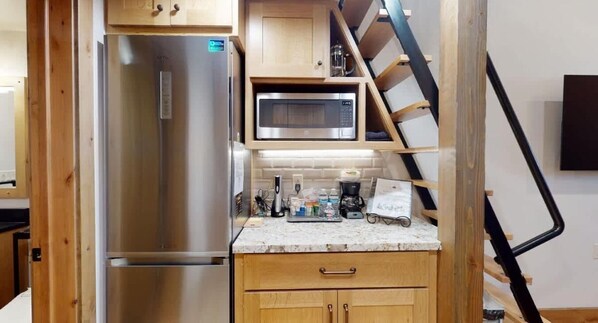 A compact kitchen with a built-in microwave, a stainless steel refrigerator, wooden cabinets, and a small countertop.