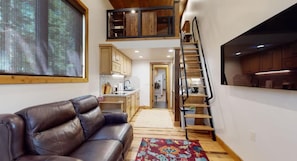 A living room with a leather sofa, a staircase, and a kitchen area. - Cozy Loft | 25 Miles to YNP | EV Charging (Island Park)