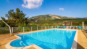 Ein Schwimmbecken mit Bergblick, umgeben von einem Zaun und Bäumen.