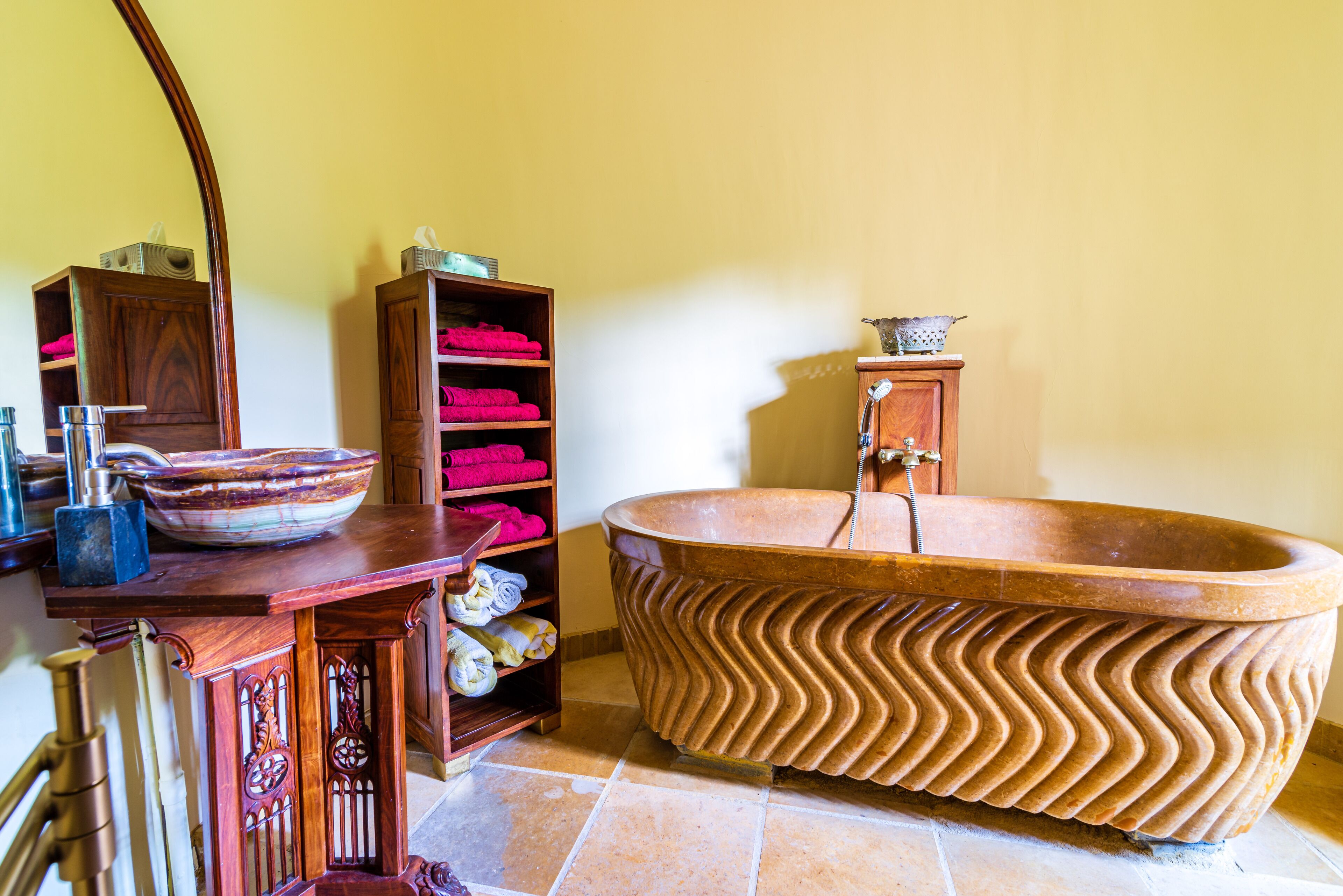 A bathroom with a large, wavy bathtub, wooden shelves with towels, and a mirror.