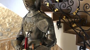 Eine Ritterstatue mit einem roten und gelben gefiederten Helm, stehend auf einer Treppe mit aufwendigen schwarzen Metallgeländern und einer Holzhandläufe.