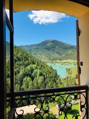 Un balcon doté d’une balustrade en métal, donnant sur un paysage montagneux avec un lac.