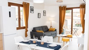 Un soggiorno moderno con un divano grigio, un tavolo da pranzo per quattro persone e un balcone con sedie gialle.