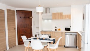 Una cucina moderna con mobili bianchi, lavastoviglie integrata e un'area pranzo con sedie bianche e una tovaglia scura.