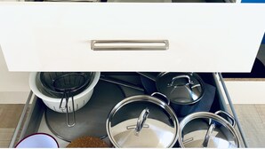 Un cajón de cocina con tiradores de acero inoxidable, que contiene utensilios y utensilios de cocina.