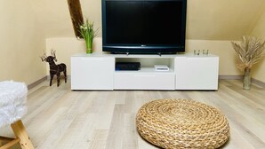 Una sala moderna con un televisor de pantalla plana sobre un mueble blanco, un otoman tejido redondo y una escultura decorativa de reno.
