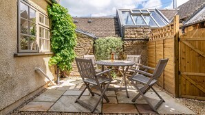 A patio with a table and chairs, a wooden fence, and a stone wall. - Poppy Cottage - sleeps 4 guests  in 2 bedrooms (Broadwell)