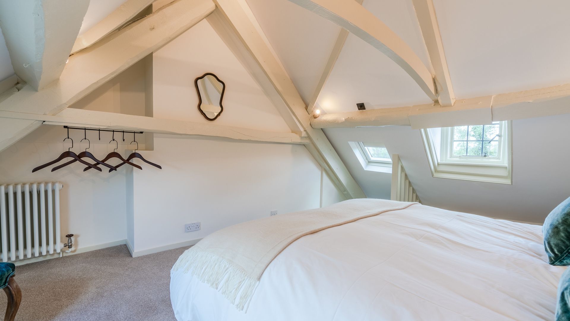Une chambre avec un plafond en pente, un lit, un radiateur et une fenêtre.