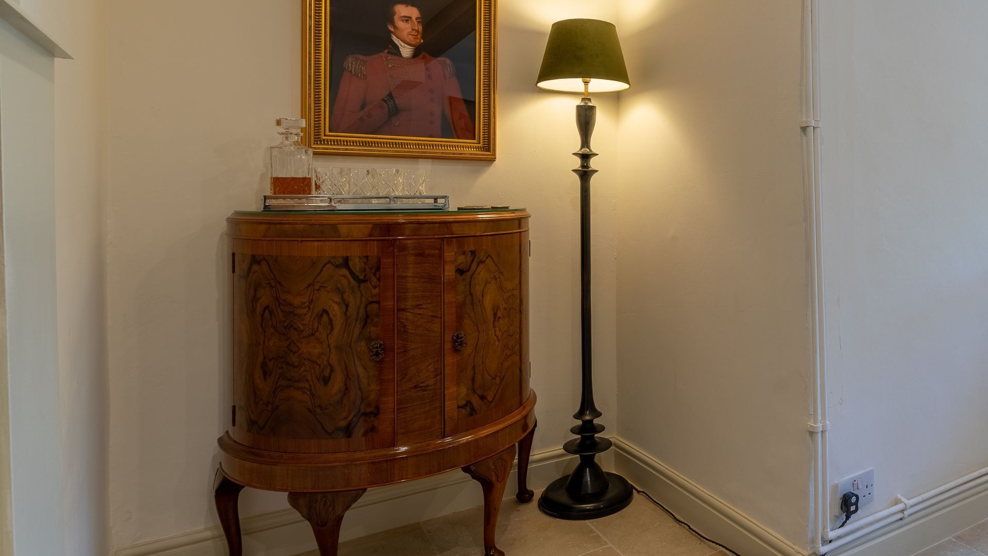 Un meuble en bois avec un dessus en verre, un portrait encadré au-dessus, et une lampe sur pied à côté.