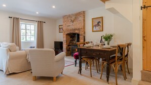 A cozy living room with a fireplace, a dining area with wooden furniture, and a comfortable sofa. - Poppy Cottage - sleeps 4 guests  in 2 bedrooms (Broadwell)