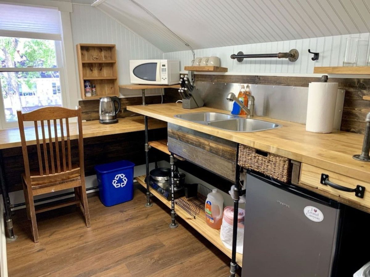 Une cuisine compacte dotée d’un plan de travail en bois, d’un évier encastré, d’un four à micro-ondes et d’un réfrigérateur.
